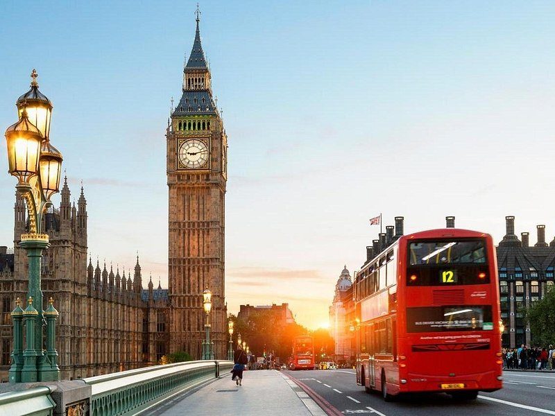 Big Ben and the Palace of Westminster at sunset, a red London bus crossing Westminster Bridge